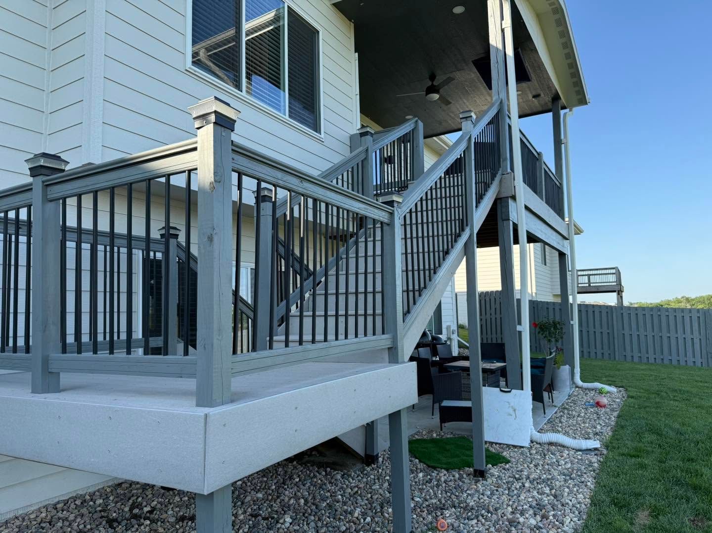Gray deck stairs and railings beside a house, with gravel landscaping and a grassy yard.