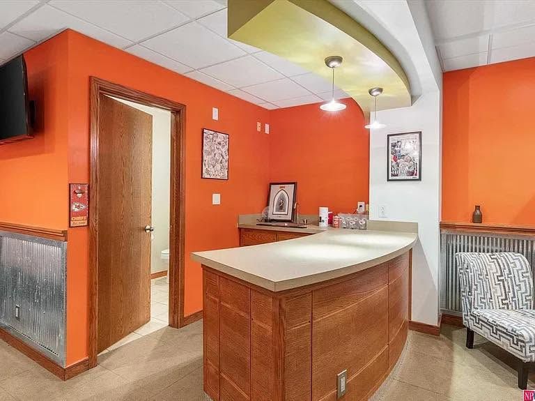 Modern lobby with orange walls, curved reception desk, and wood-paneled elevator area