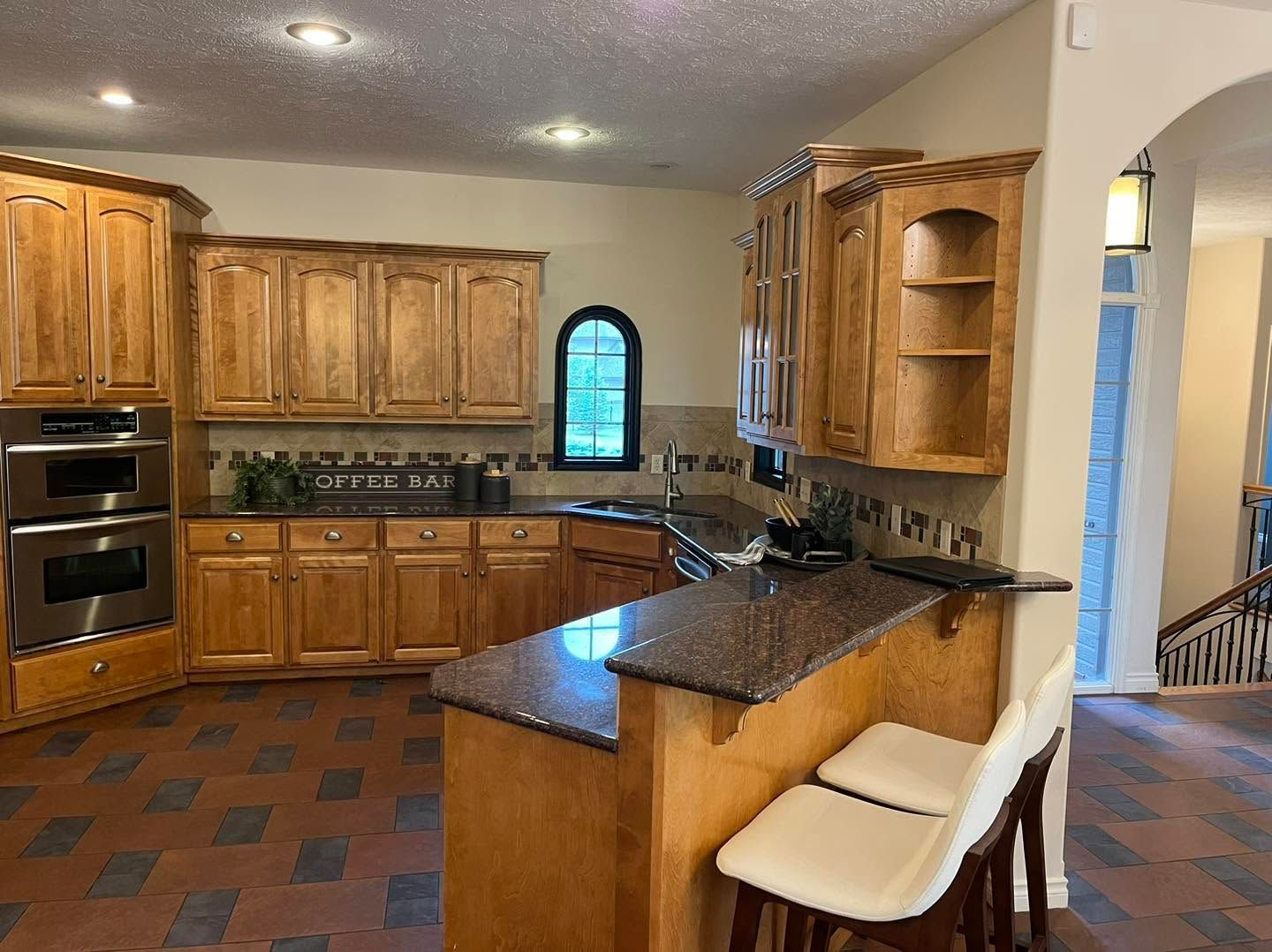 Spacious kitchen with wood cabinets, dark countertops, tiled floor, and a breakfast bar with stools.