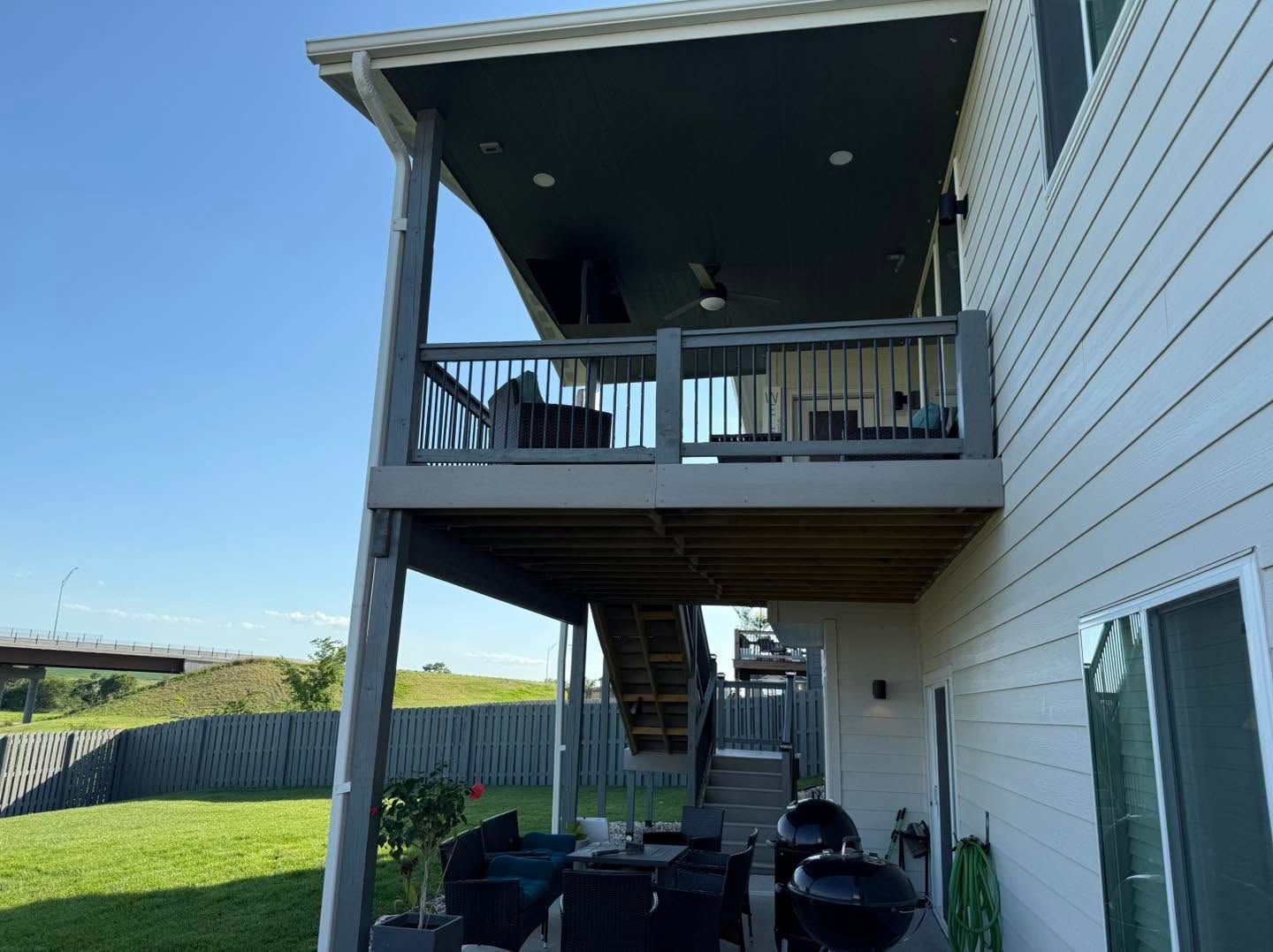 Two-story house with upper and lower decks, outdoor furniture, and a grassy yard.