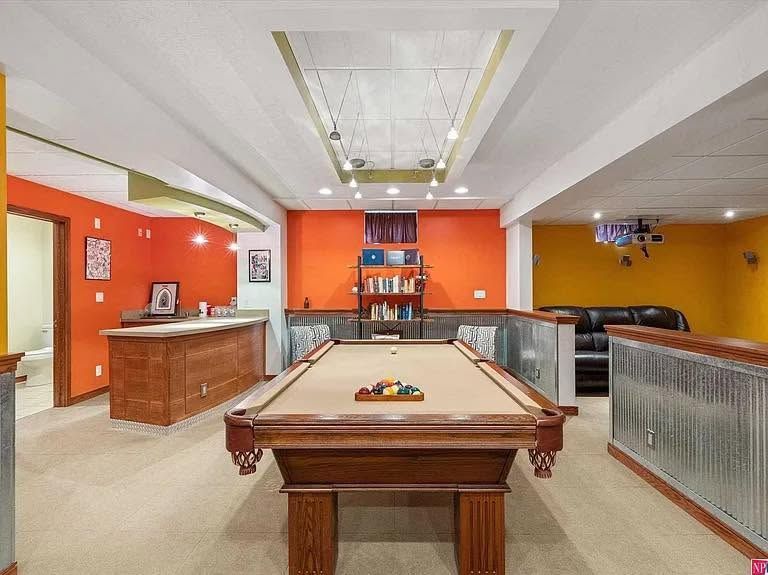 Pool table in a brightly lit recreation room with orange walls, bar counter, and seating area