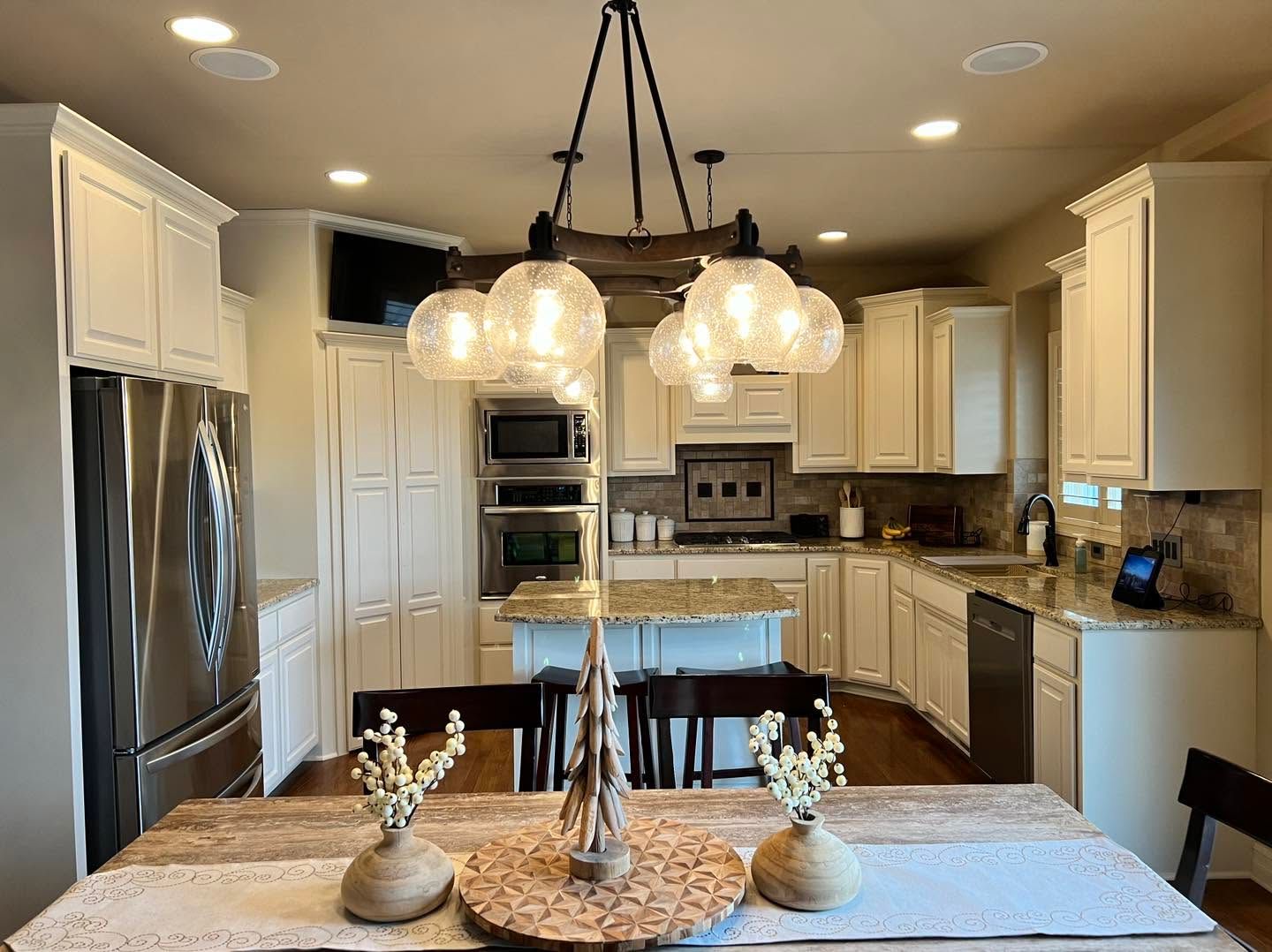 Bright kitchen with white cabinets, stainless appliances, pendant lights, and a dining table in the foreground