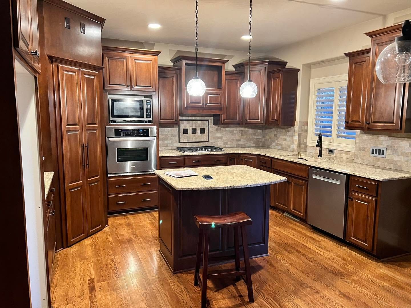 Warm kitchen with dark wood cabinets, granite island, stainless appliances, and hardwood floors.