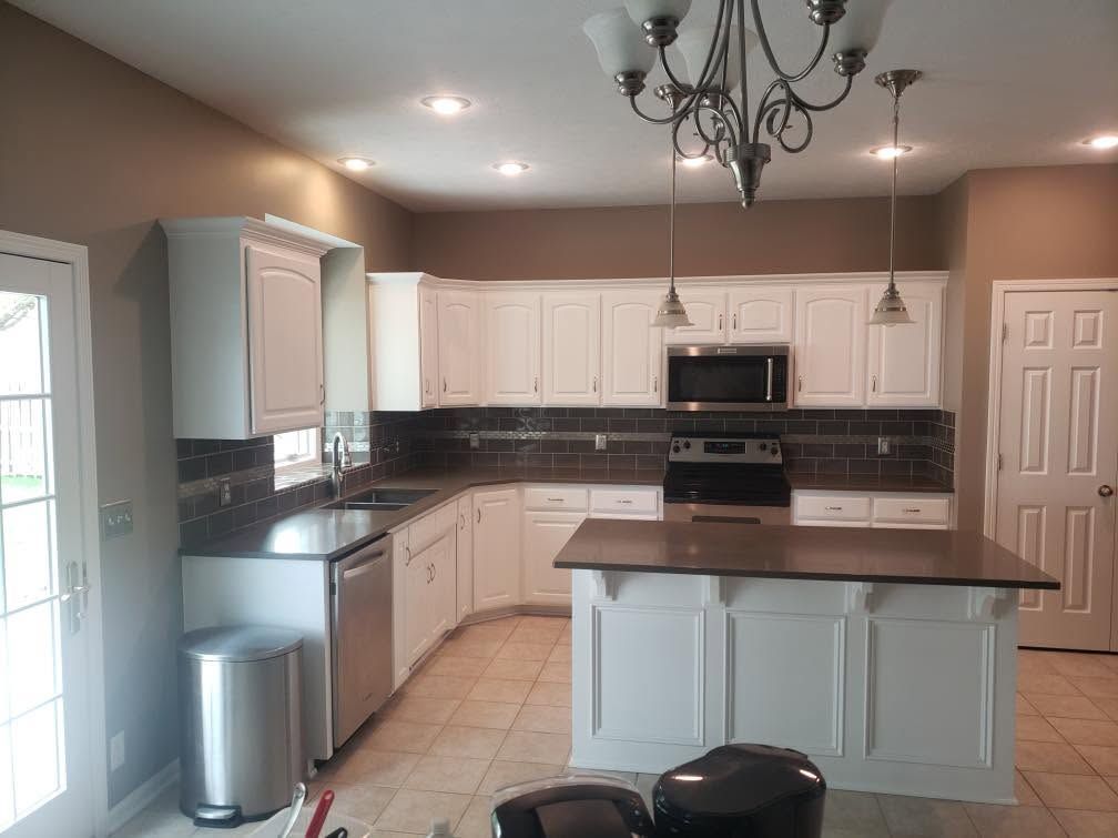 Bright modern kitchen with white cabinets, dark countertops, and a central island under a chandelier.