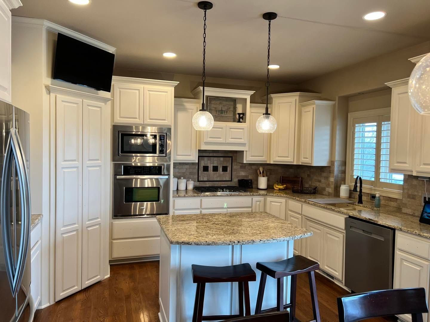 Bright kitchen with white cabinets, granite island, pendant lights, and stainless steel appliances.
