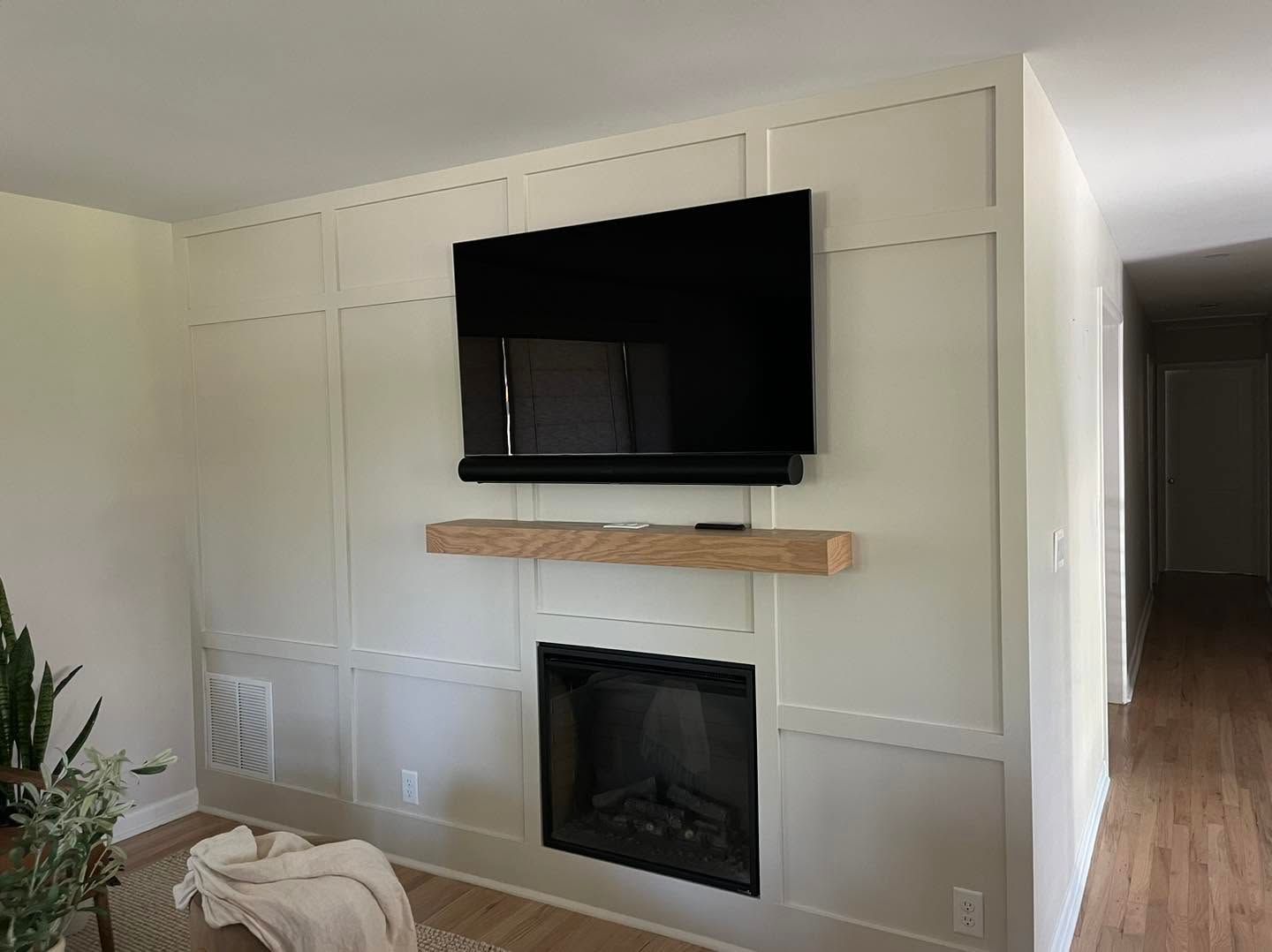 Living room wall with mounted TV, floating shelf, and black fireplace on a white paneled accent wall