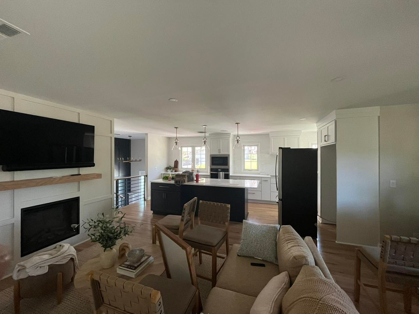Bright open living room with beige sofa, fireplace, wall TV, and kitchen in the background