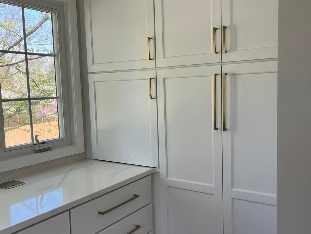 Bright white kitchen cabinets and a window overlooking trees, with a built-in countertop beneath.