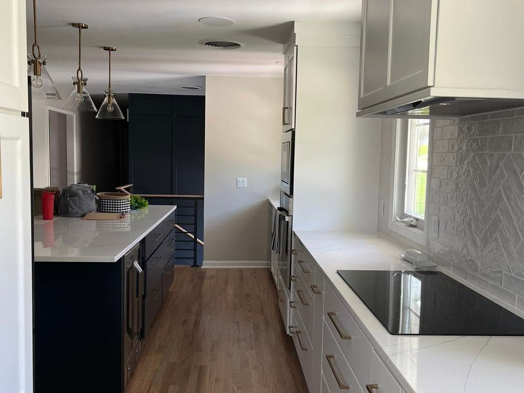 Narrow modern kitchen with white cabinets, dark counters, and a window over the sink.