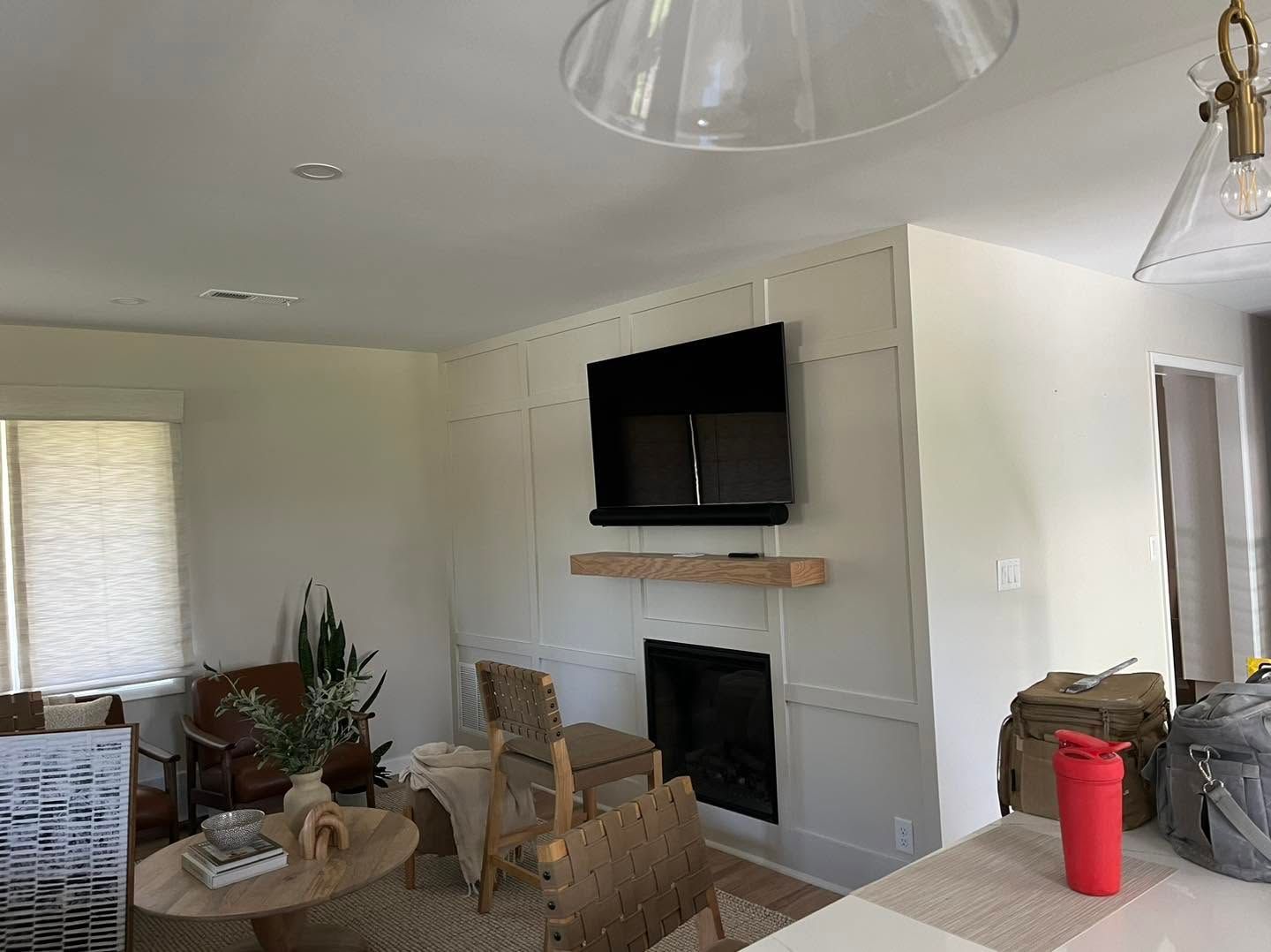 Modern living room with wall-mounted TV above fireplace, wicker chairs, and red tumbler on a side table