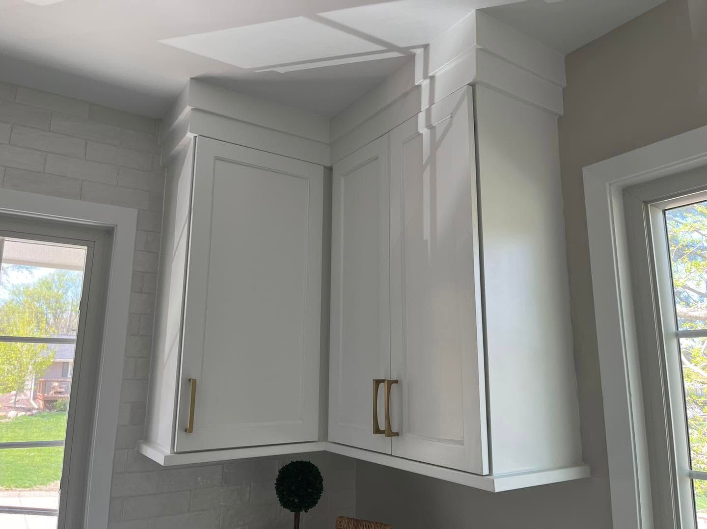 White corner kitchen cabinets with brass handles beside two windows and daylight.