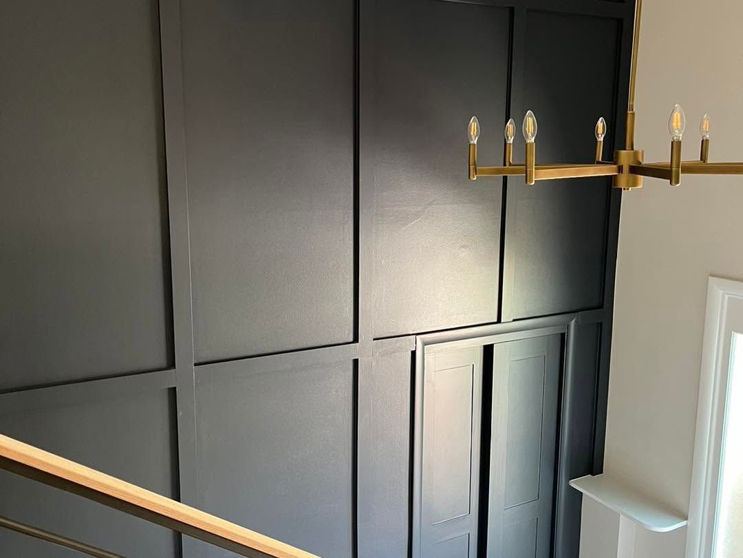 Modern interior with dark paneled wall, gold chandelier, and staircase railing