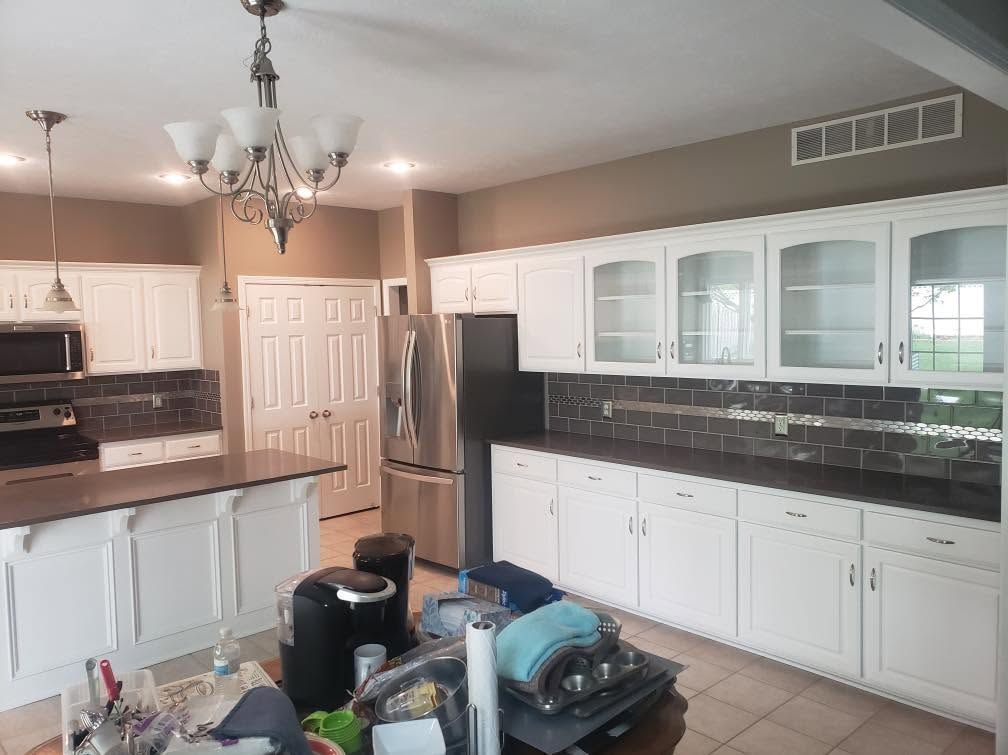 Bright kitchen with white cabinets, black countertops, stainless fridge, and a chandelier over the island.