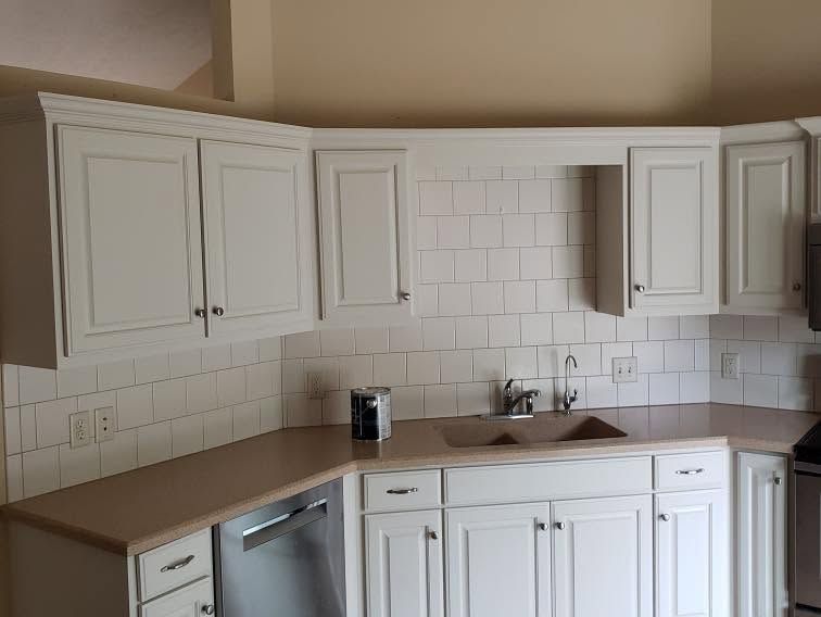 White kitchen with cabinets, beige countertops, tiled backsplash, sink, and dishwasher