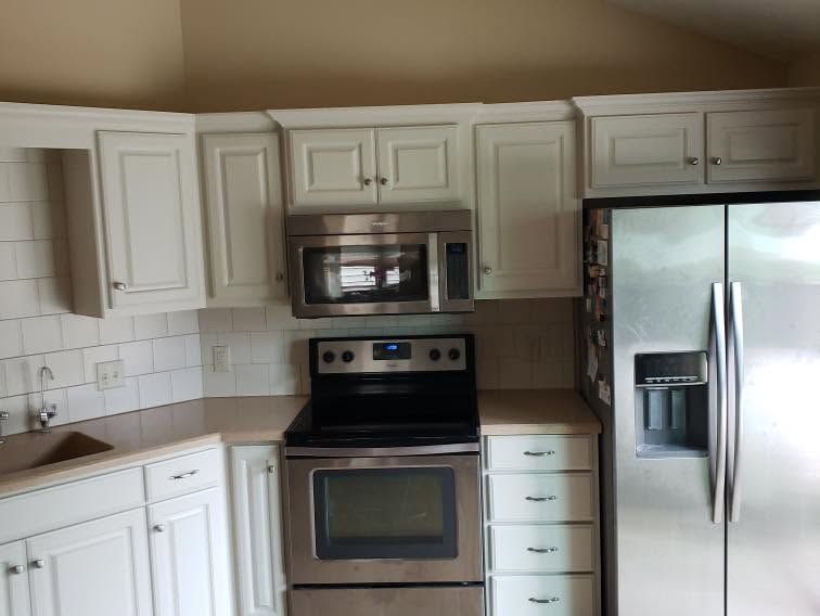 White kitchen with stainless steel appliances, tiled backsplash, and beige countertops