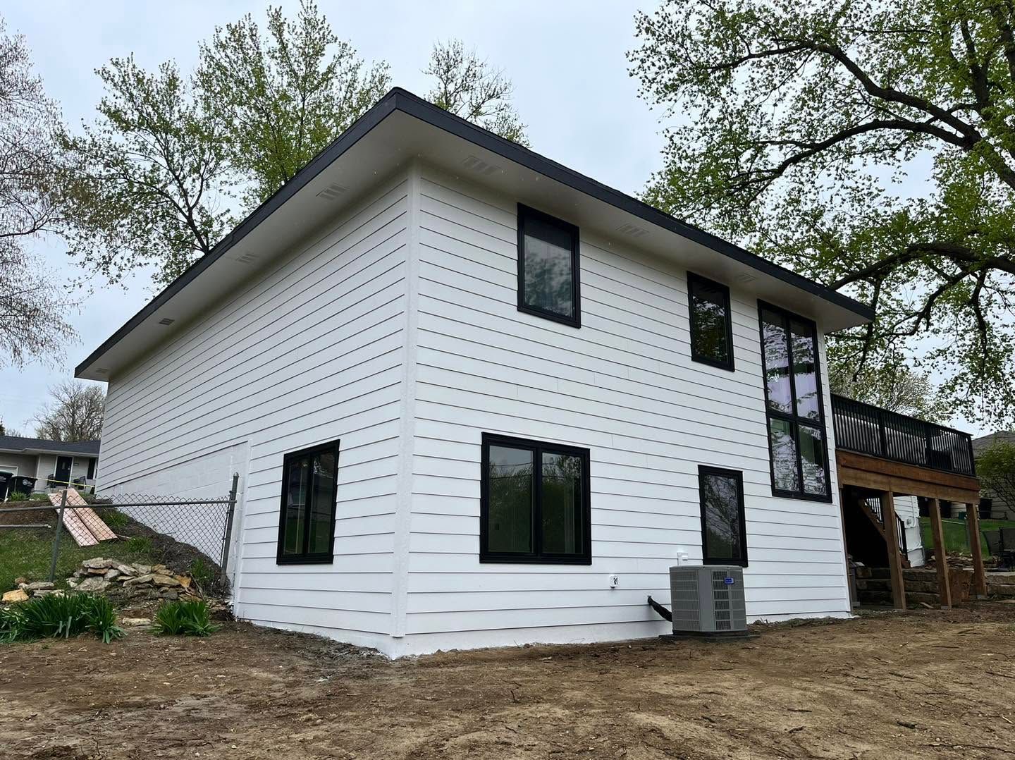 White two-story house with black-trimmed windows and a covered porch under construction.