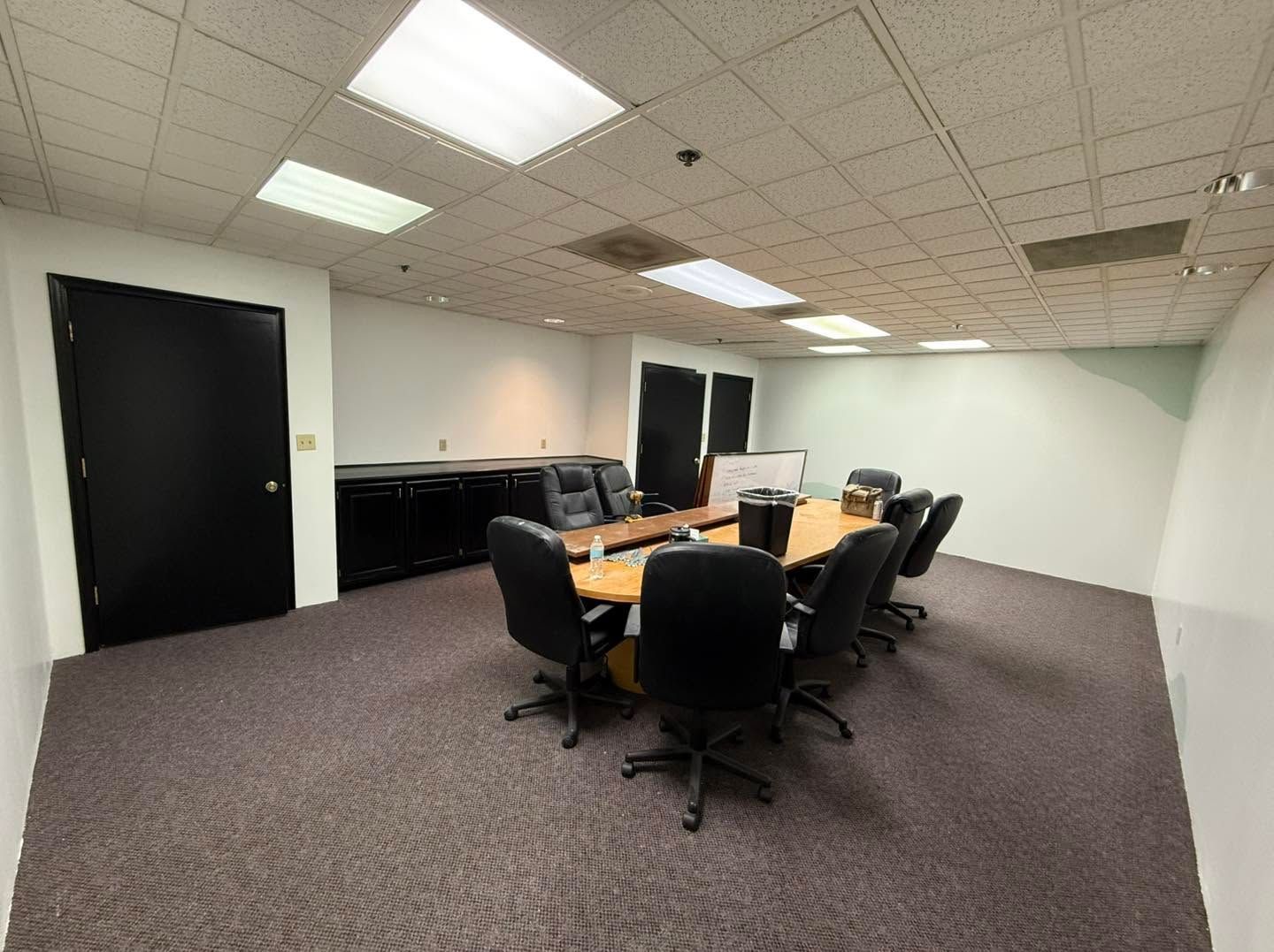Empty conference room with black chairs around a wooden table and beige carpet under fluorescent ceiling lights