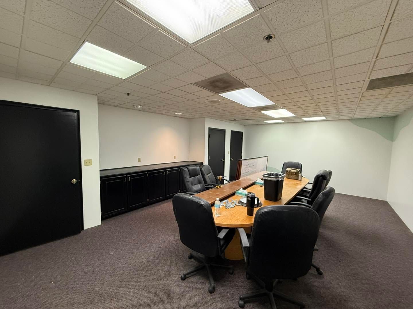Empty conference room with black chairs, wooden table, cabinets, and fluorescent ceiling lights