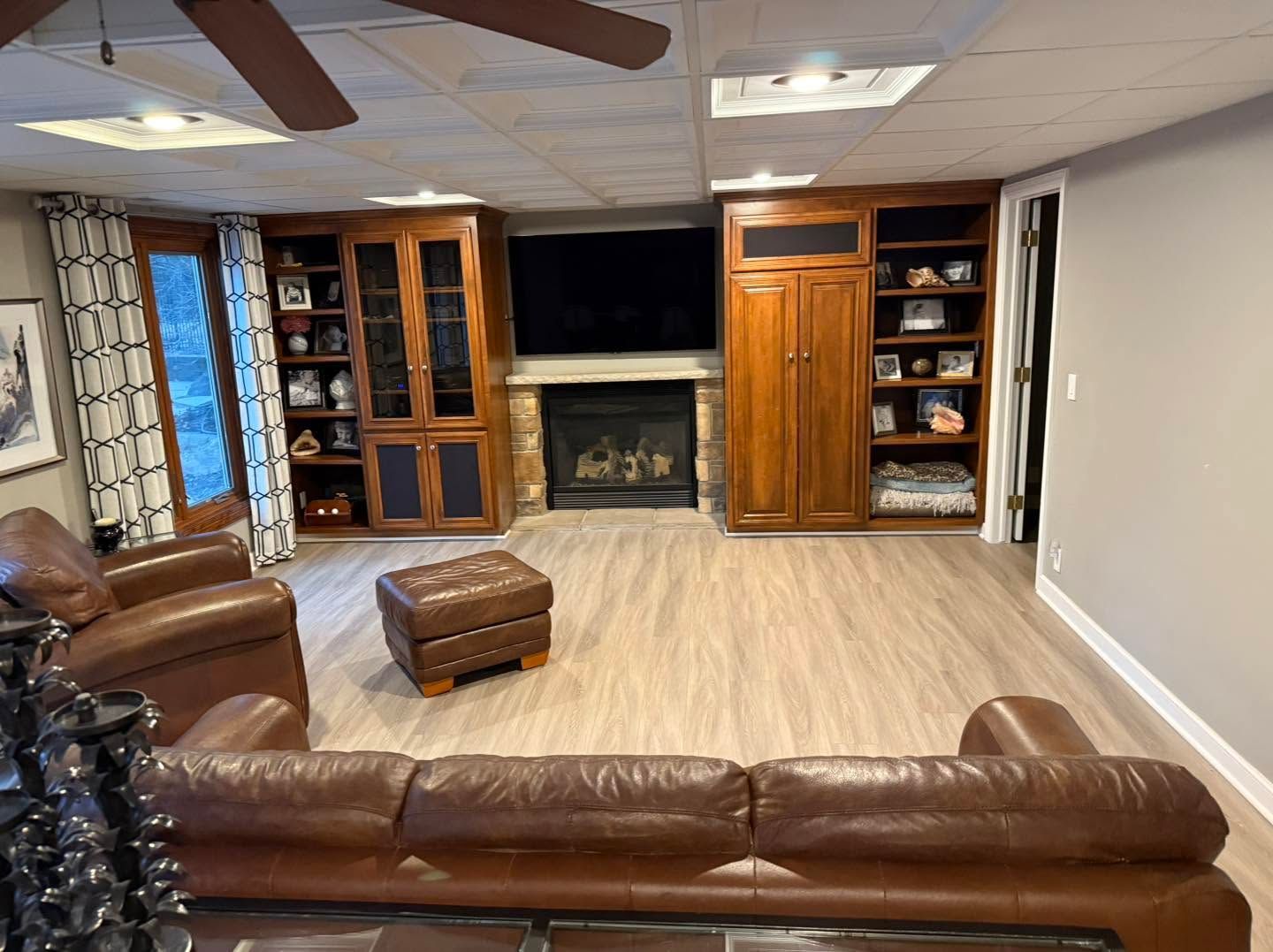 Living room with brown leather sofa, ottoman, fireplace, built-in shelves, and ceiling fan