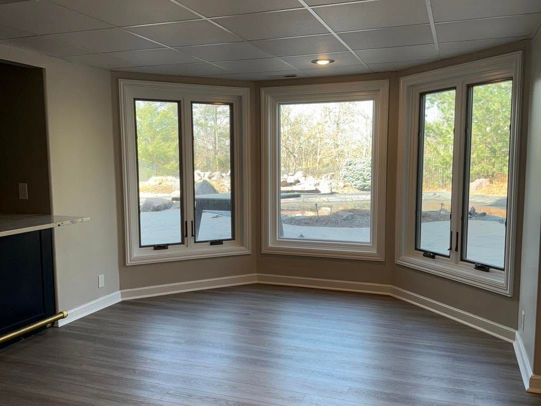 Empty room with curved bay windows, beige walls, and wood-look flooring overlooking a snowy outdoors