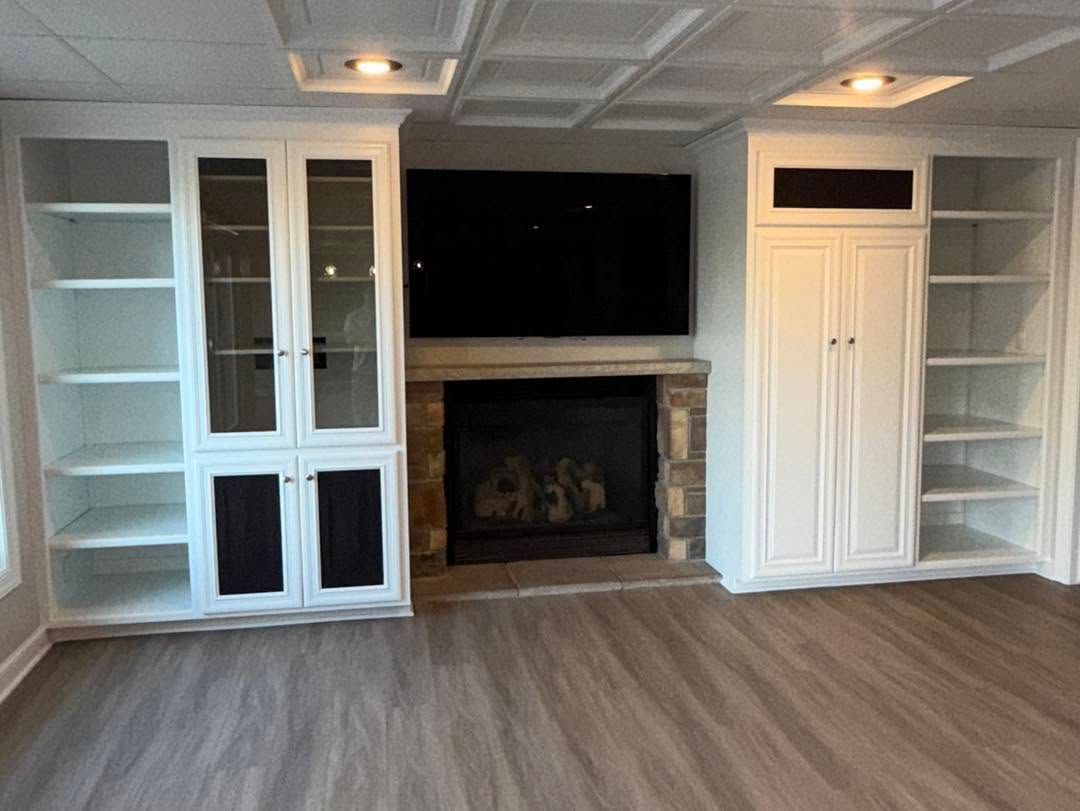 Living room wall with built-in shelves, cabinets, fireplace, wall-mounted TV, and wood flooring