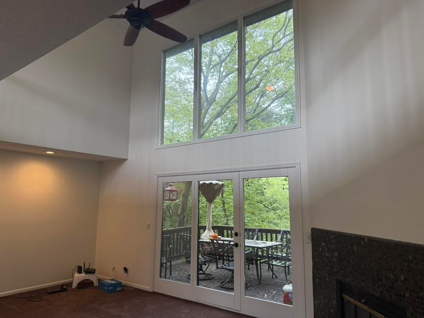 Bright living room with high windows, ceiling fan, and glass doors opening to a patio.