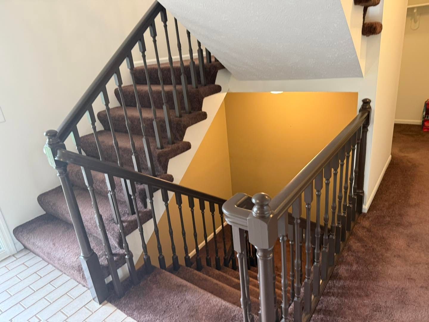 Indoor staircase with dark wood banister, carpeted steps, and a yellow stairwell wall
