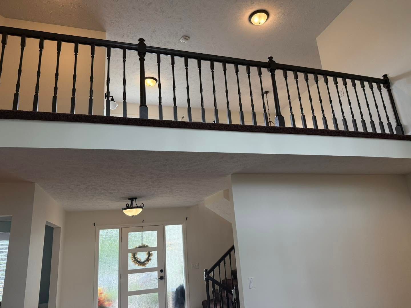 Interior view of a home with a loft railing, staircase, and front door under warm ceiling lights