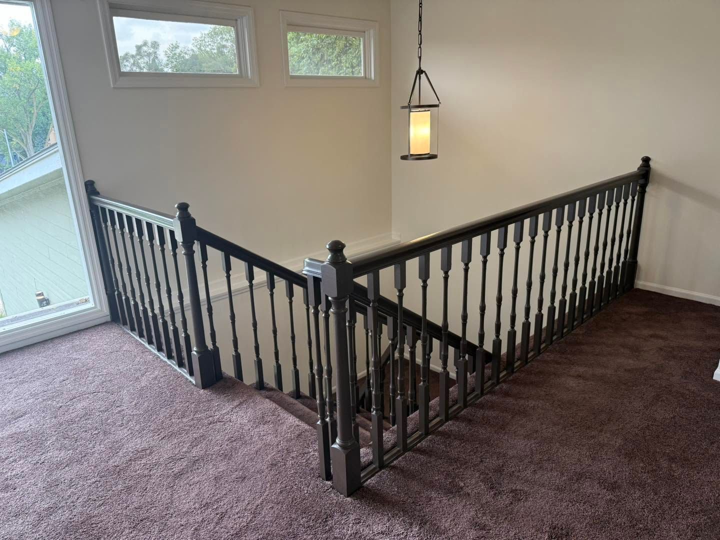 Interior staircase landing with black railings, beige walls, carpet, and hanging lantern light