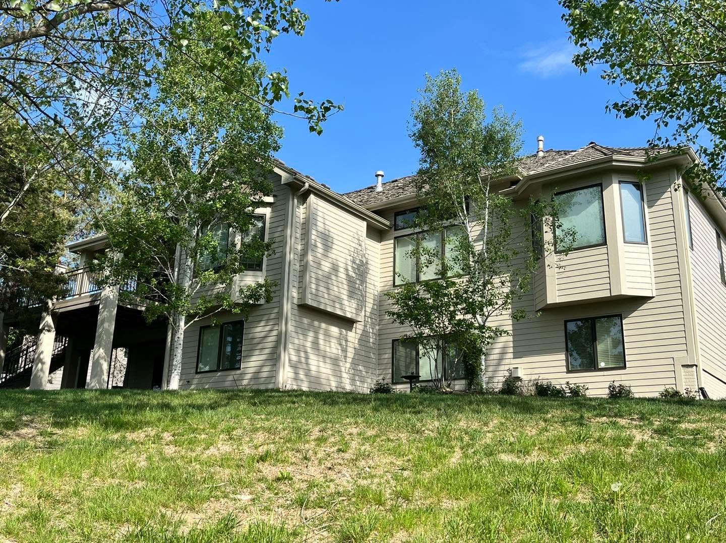Apartment building behind trees on a grassy slope under a blue sky