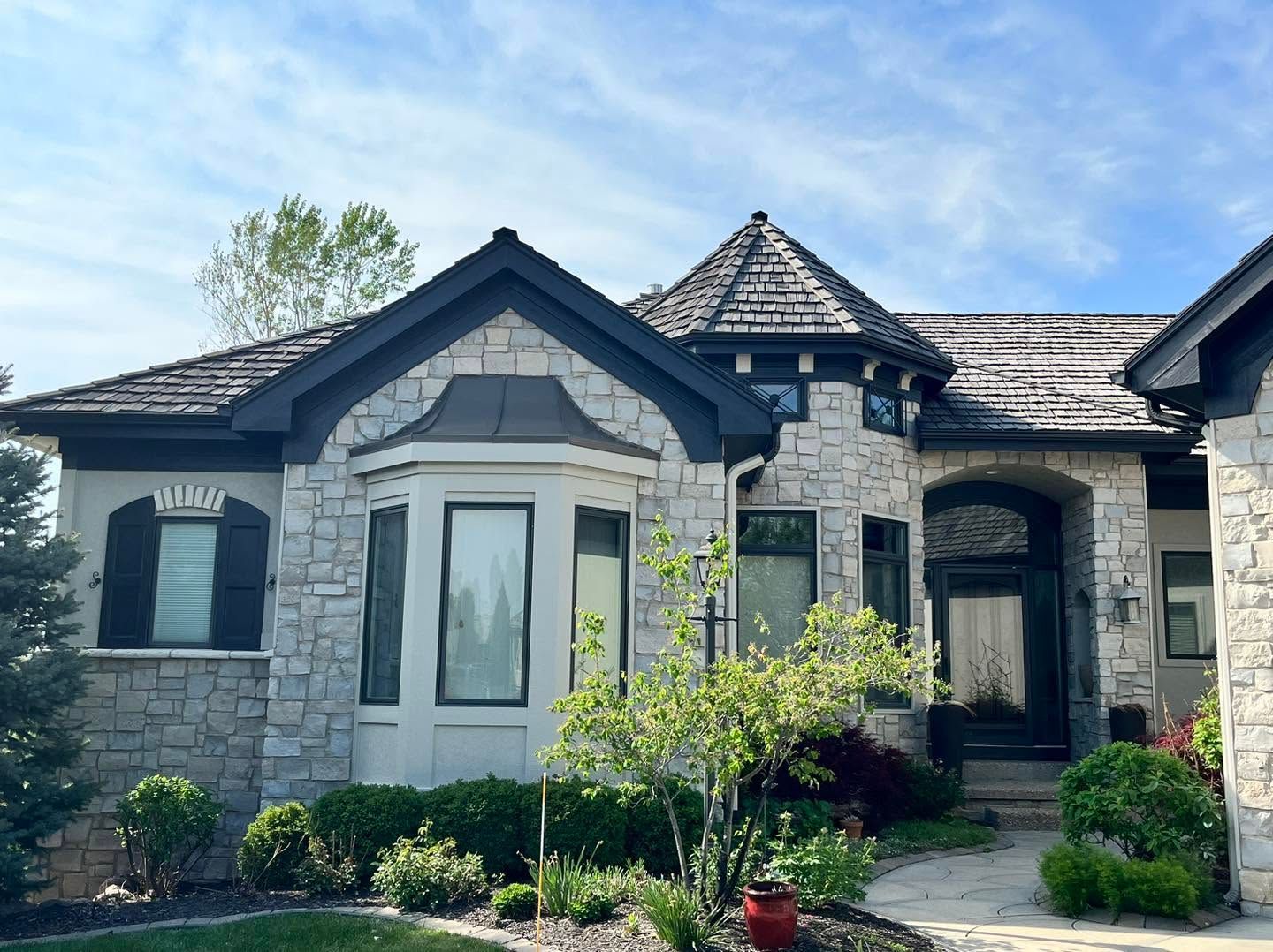 Stone house with dark gray roof, arched windows, and a small front garden under a blue sky