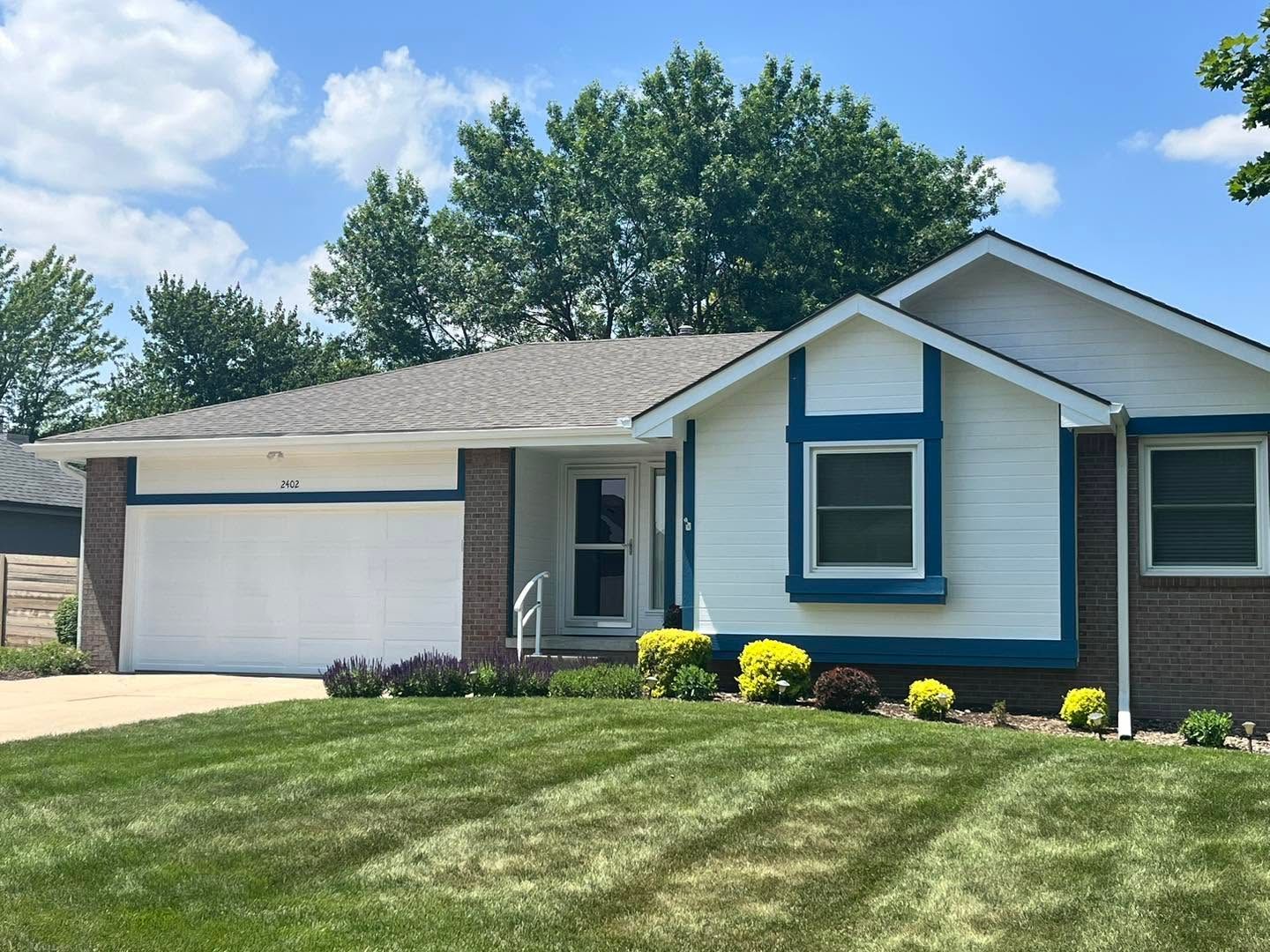 Suburban single-story house with white siding, blue trim, and a two-car garage on a sunny day