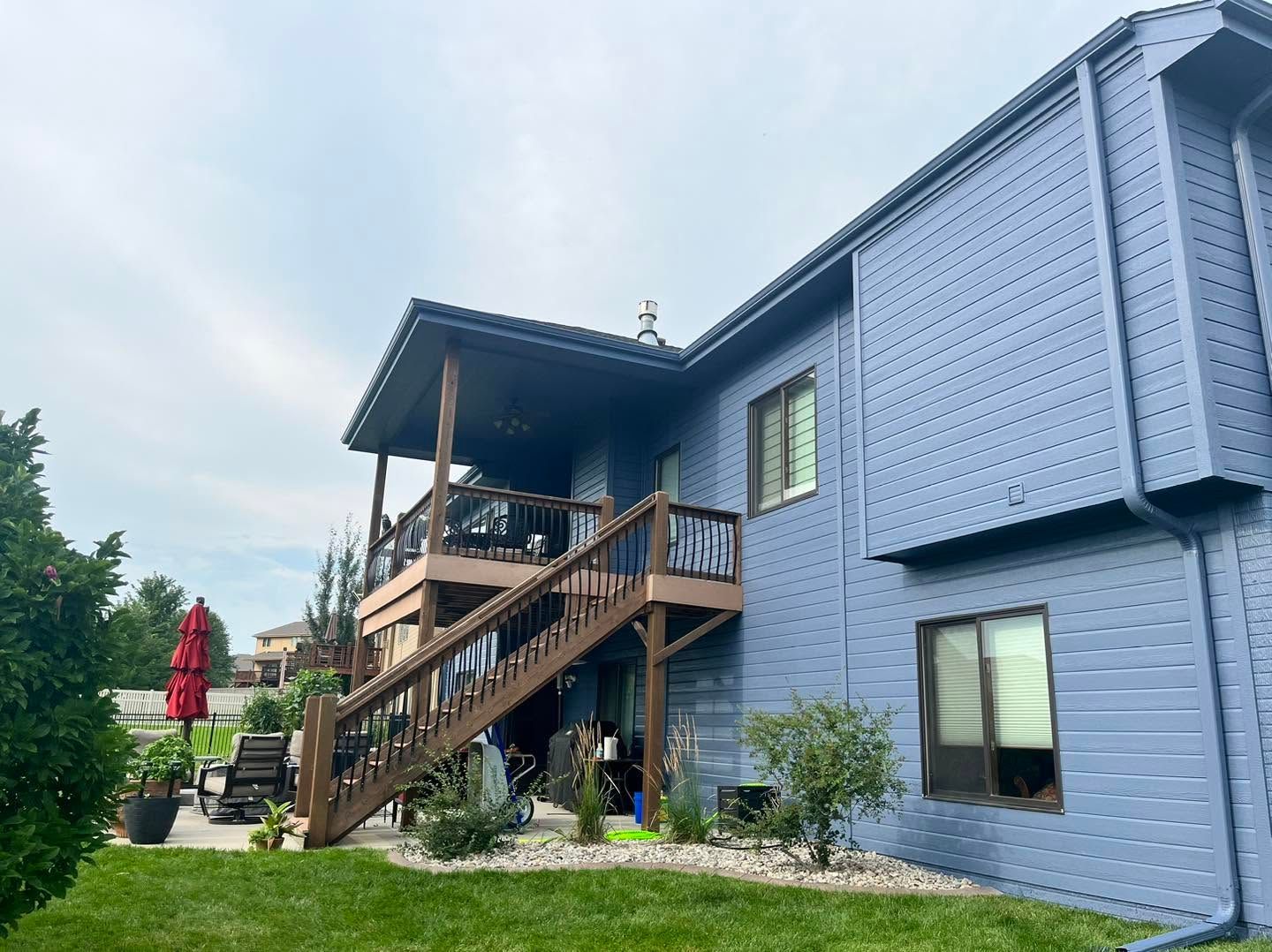 Blue house with wooden stairway and porch, seen from a grassy yard under a cloudy sky