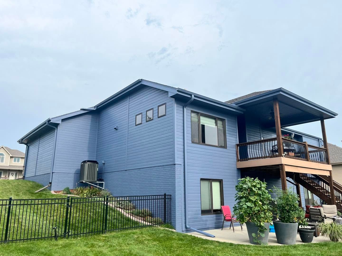 Blue two-story house with a covered porch and stairs on a grassy lot under a cloudy sky