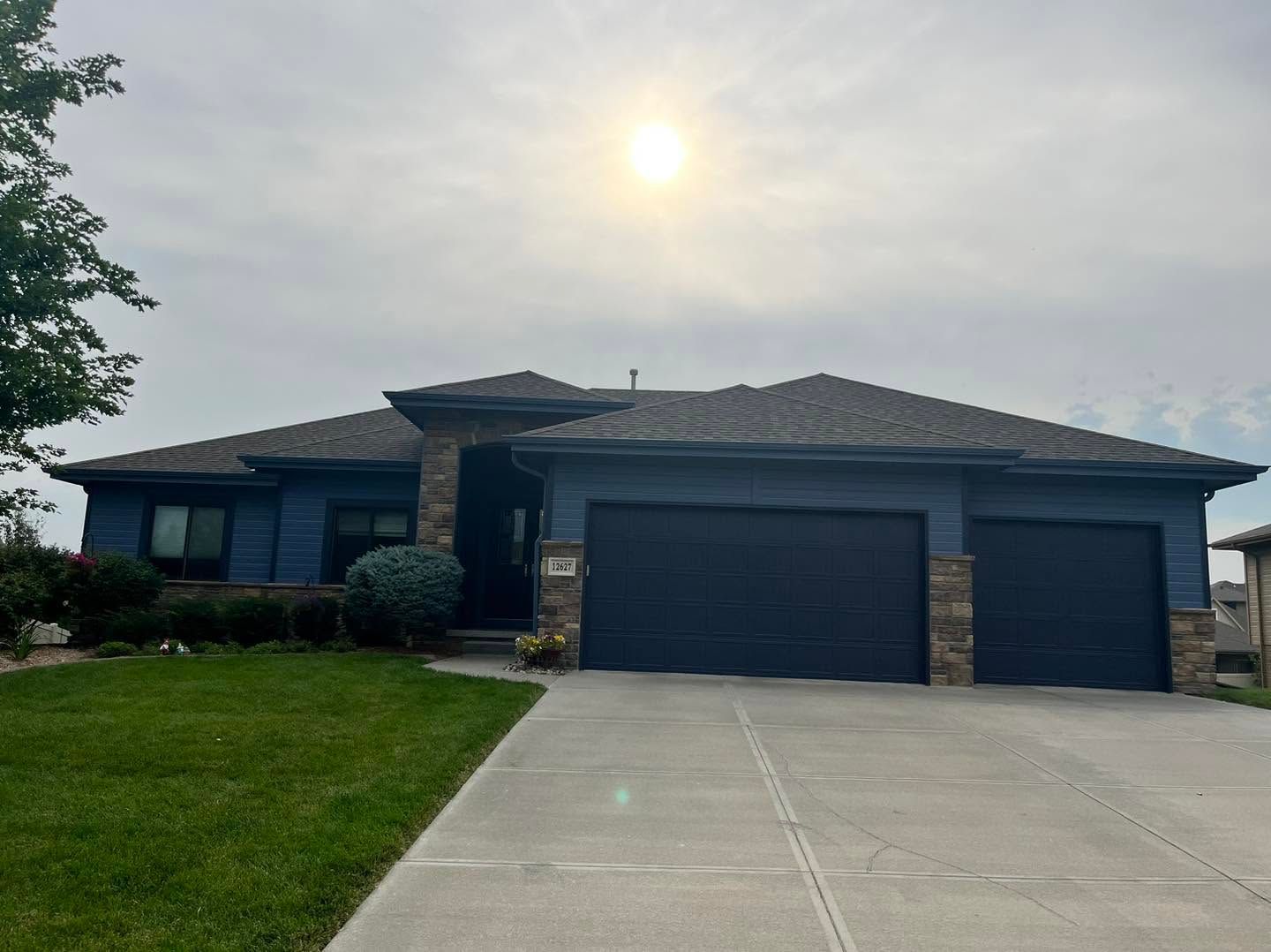 Single-story dark brick house with a two-car garage and concrete driveway under a bright sun.