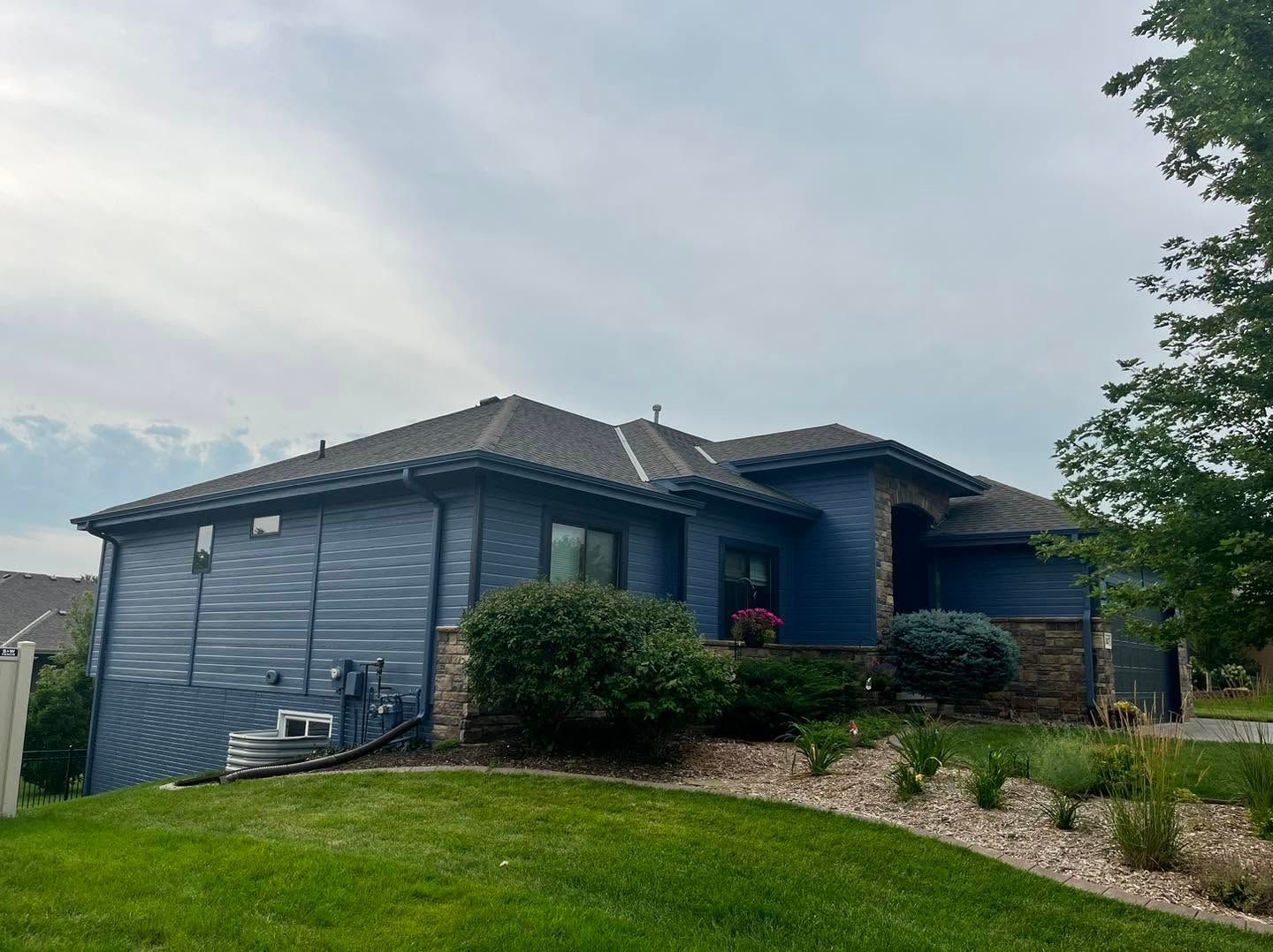 Blue single-story house with gray roof and landscaped front yard under a cloudy sky