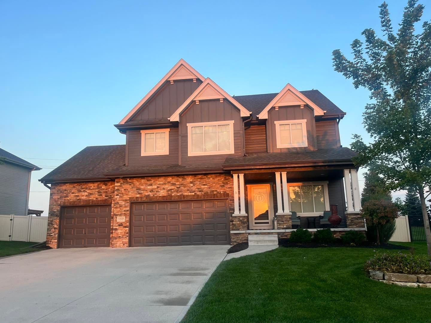 Two-story brick house with a three-car garage and front lawn at sunset