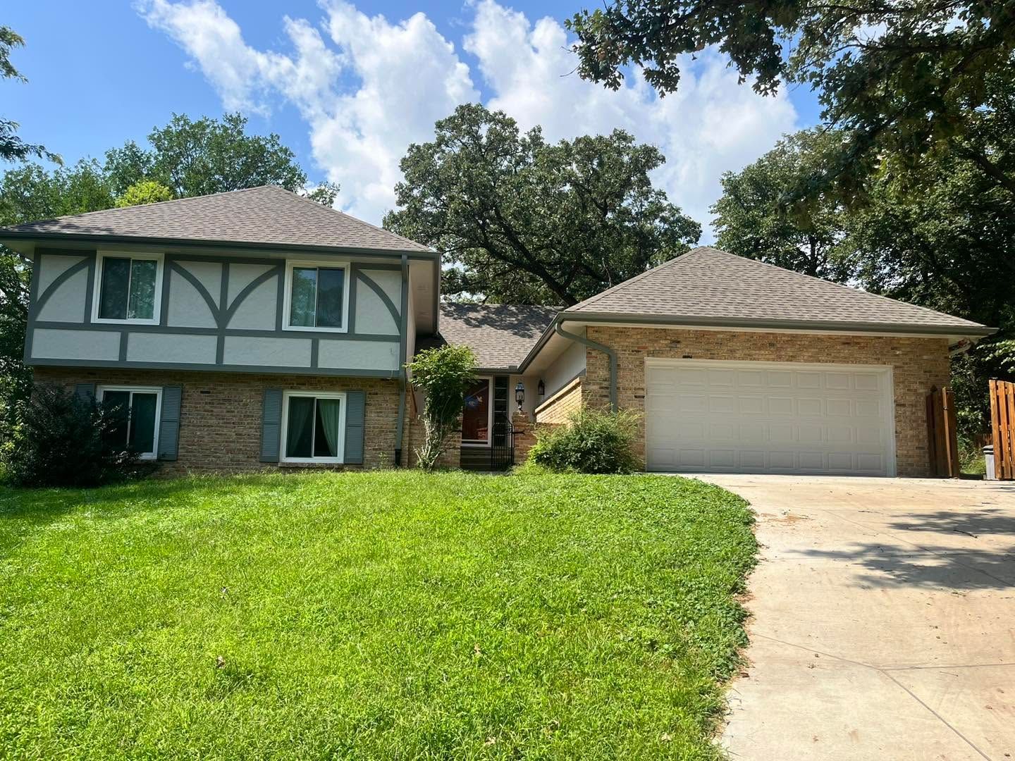 Suburban two-story house with a two-car garage, green lawn, and partly cloudy sky.
