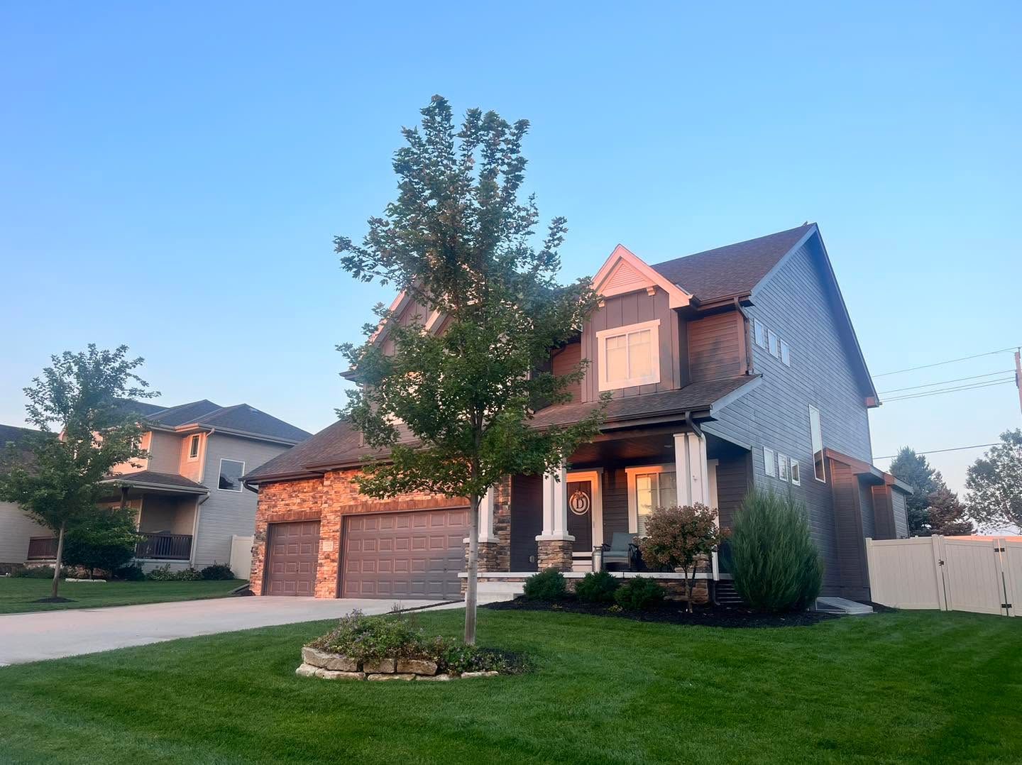 Suburban two-story house with a garage, front porch, and tree at dusk