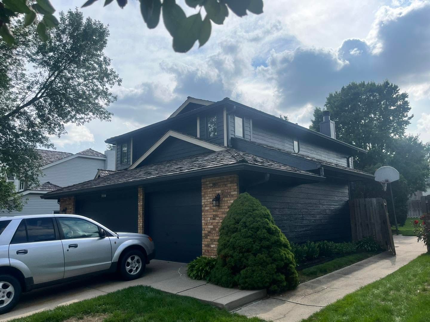 Suburban house with stone accents, a parked silver SUV, and trees along the sidewalk under a cloudy sky