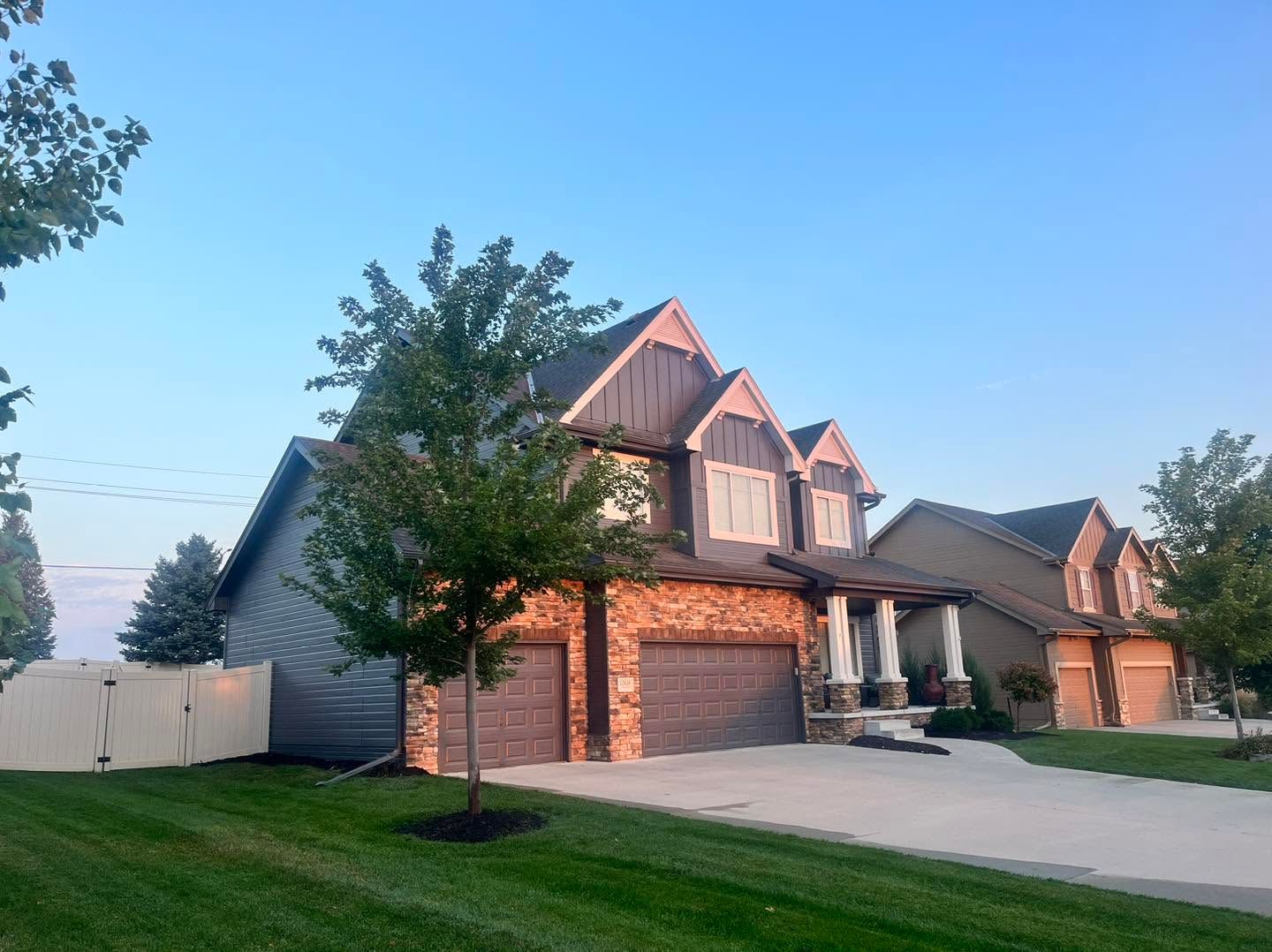 Suburban brick house with dormer windows and a driveway at dusk