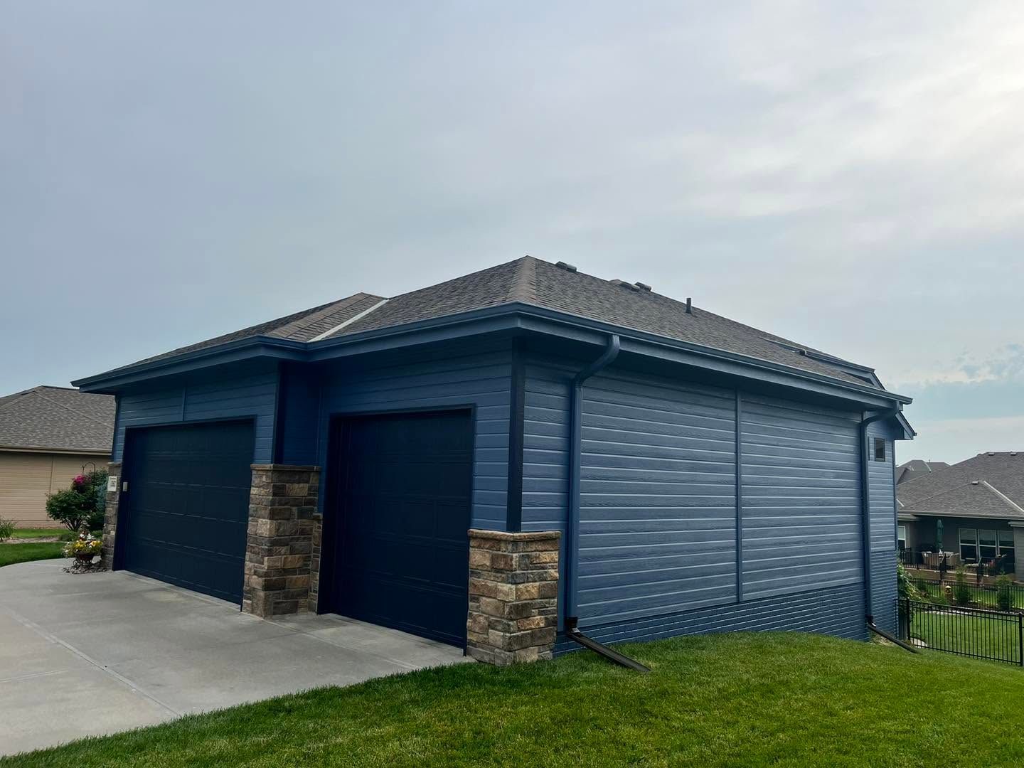 Blue double garage with stone pillars and closed roller doors in a suburban driveway.