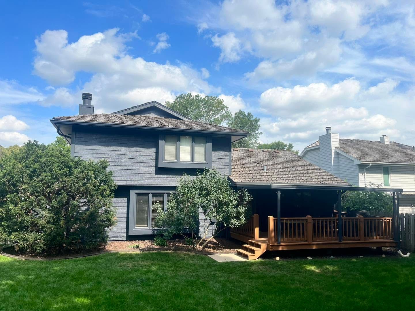 Two-story gray house with a wooden porch and green lawn under a blue sky