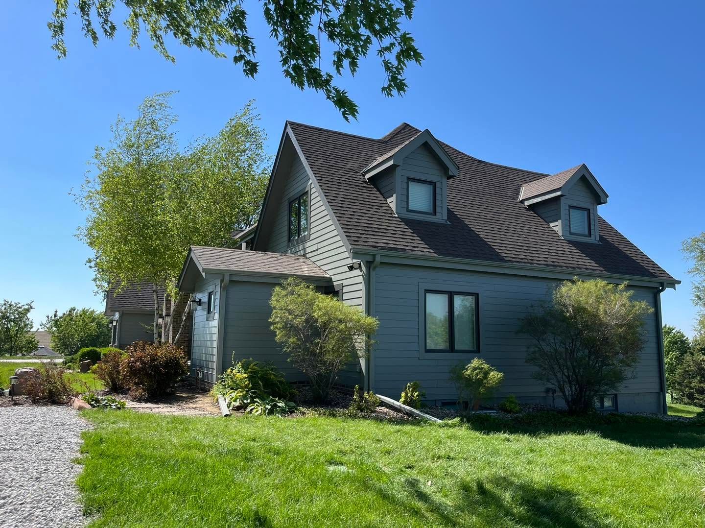 Brick house with dark roof and green lawn under a bright blue sky
