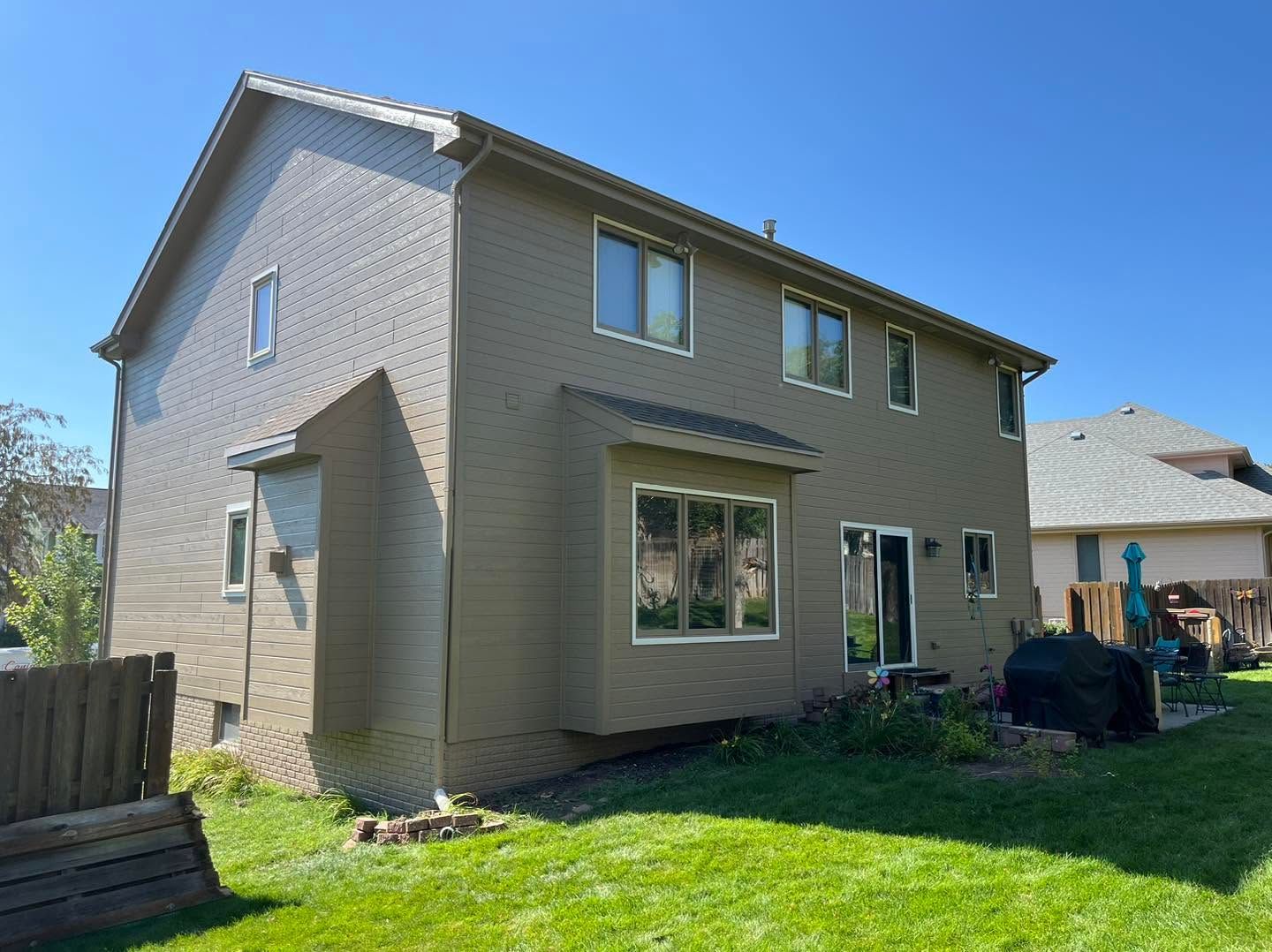 Two-story beige house with a fenced backyard, green lawn, and bright blue sky