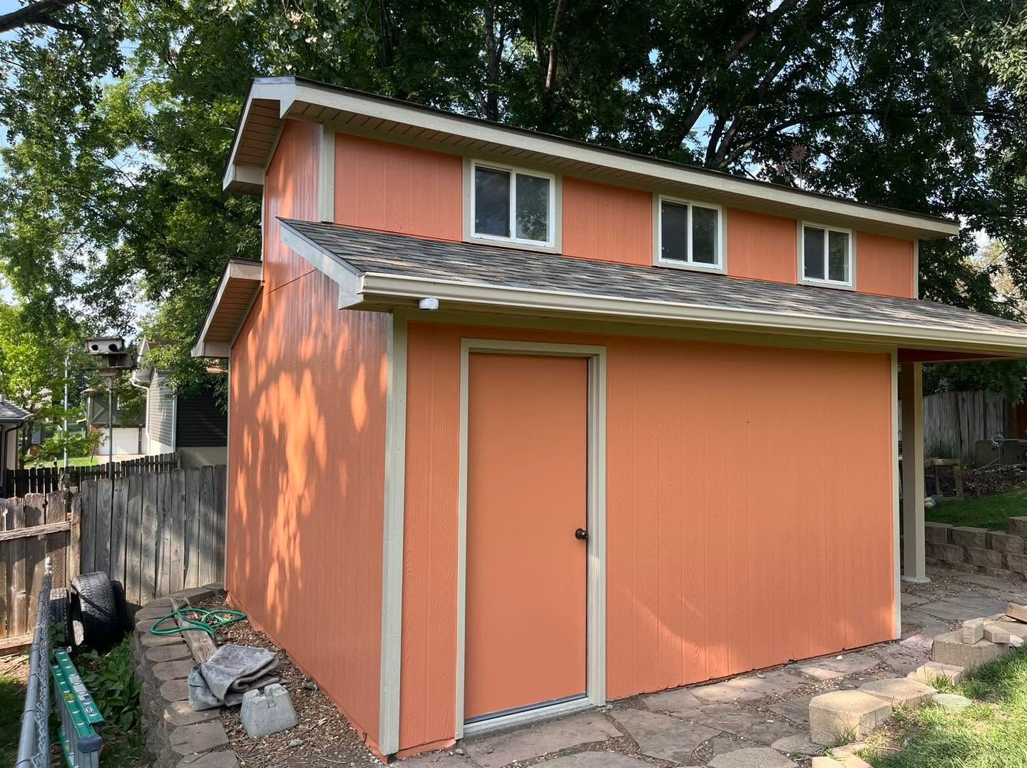 Orange garden shed with a sloped roof and small windows beside a fence and trees