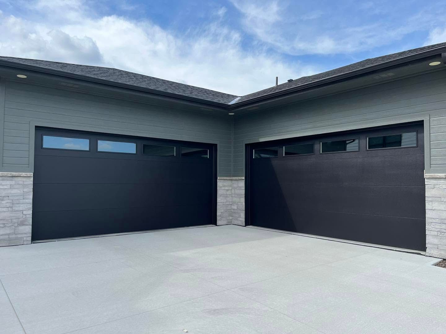 Modern home exterior with two black garage doors and a light concrete driveway under a cloudy sky