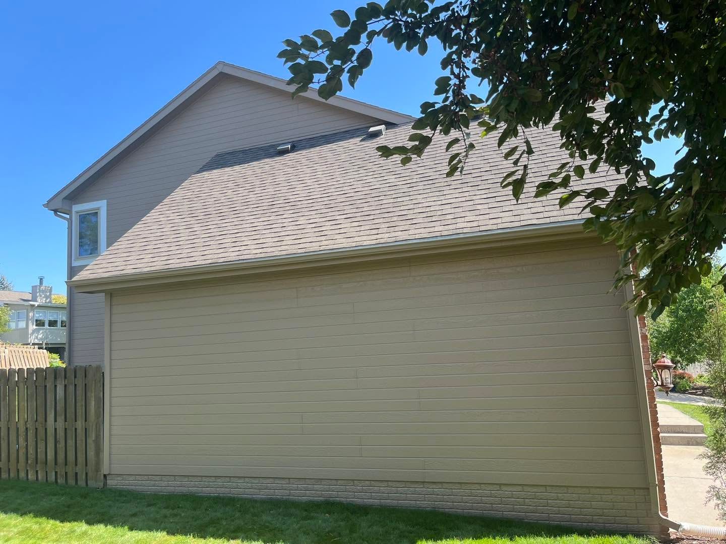 Beige house exterior with sloped roof, viewed from the side under a leafy tree.
