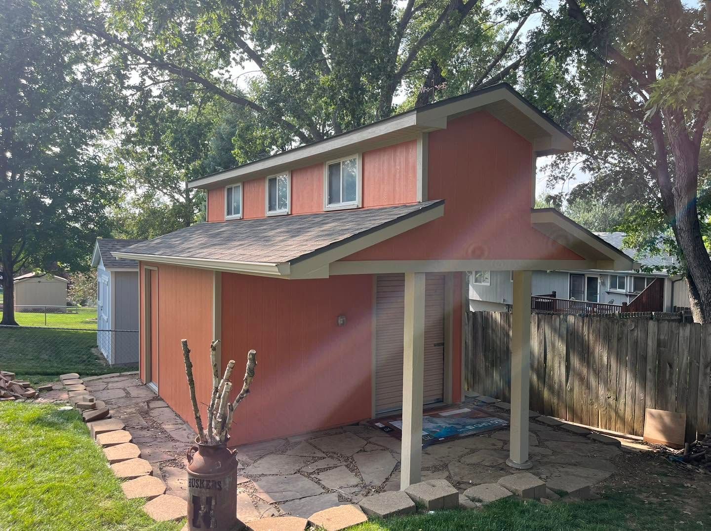Small pink house with a slanted roof and screened porch, surrounded by trees and a wooden fence.