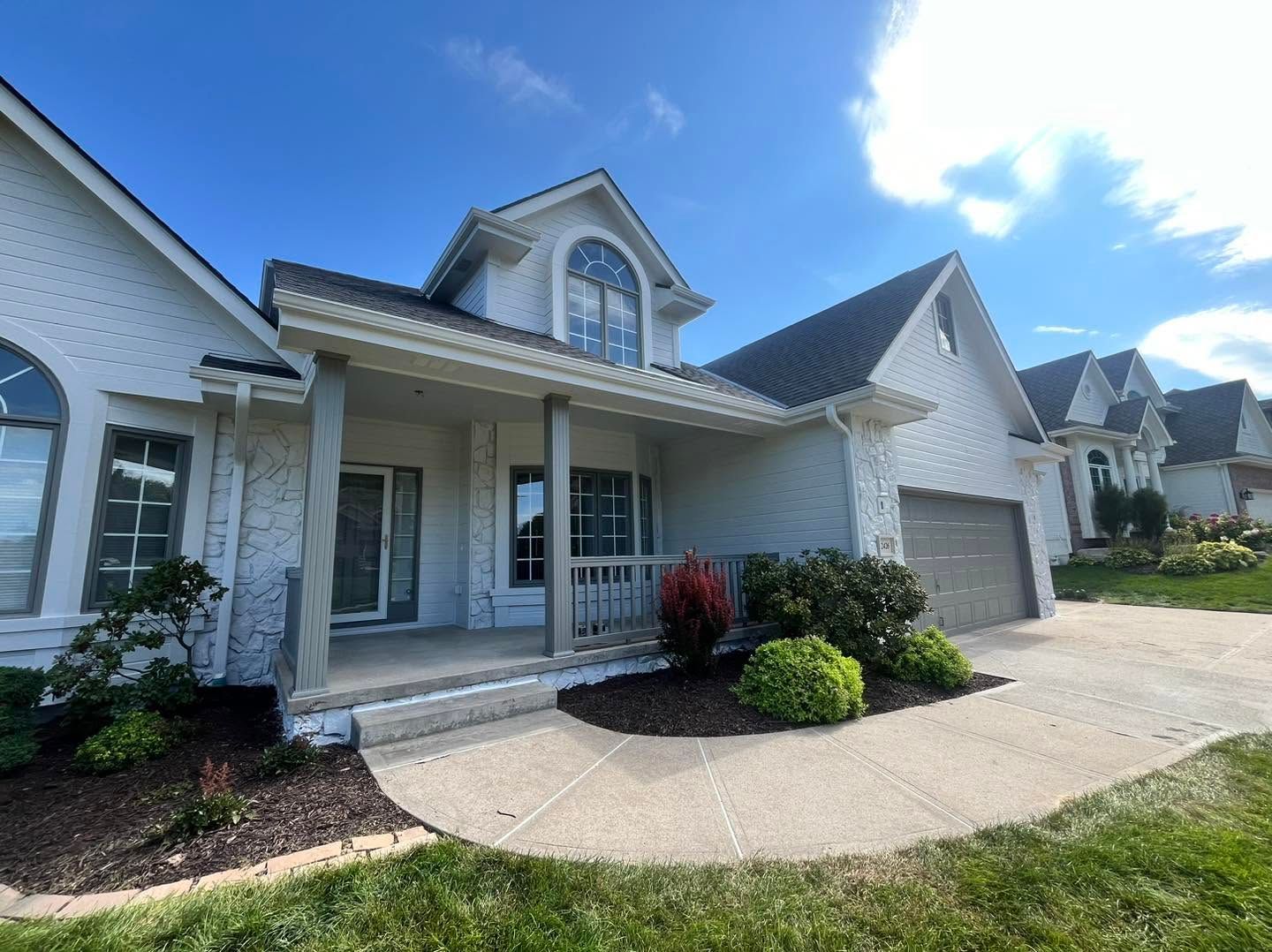 Suburban house exterior with white siding, front porch, garage, and a curved driveway under a blue sky